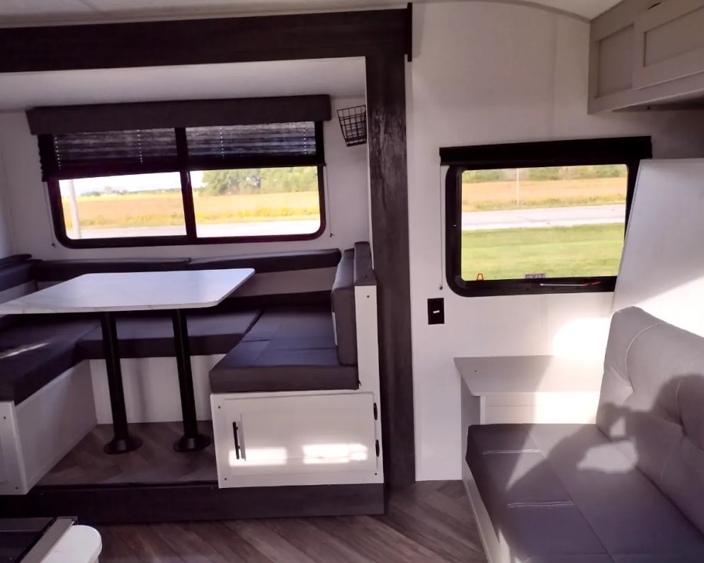 Spacious RV rental interior featuring a dinette, comfortable seating, and large windows with scenic outdoor views. Ideal for travel.