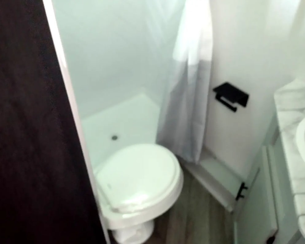 RV rental interior: A clean, white bathroom featuring a toilet, stand-up shower with curtain, and a sink with vanity.