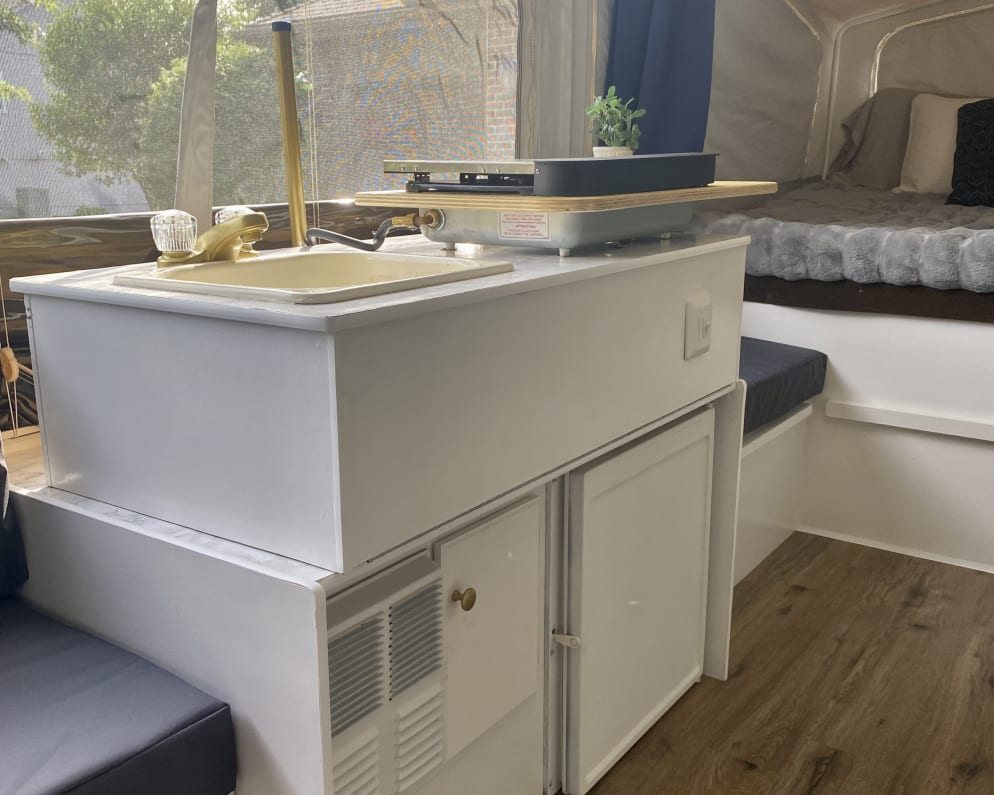 An rv rental interior featuring a compact kitchen with a sink/stove, a cozy bed, and an AC unit for adventures.
