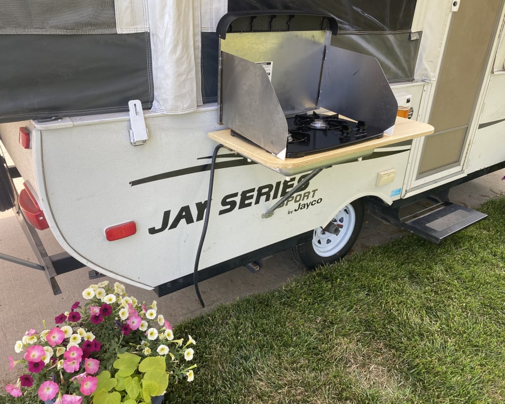 RV rental: Exterior view of a pop-up camper with an attached outdoor stove, ready for outdoor cooking and camping meals.