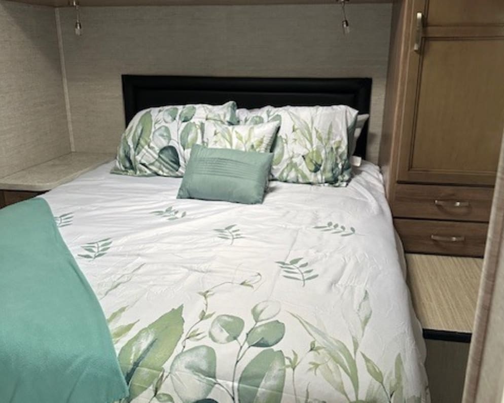 title='Contact us now about this 2021 Jayco Redhawk SE Class C RV for Rent in Fort Wayne, Indiana rental unit!' Cozy RV rental bedroom with nature-themed bedding, a comfortable bed, and wood overhead cabinets.