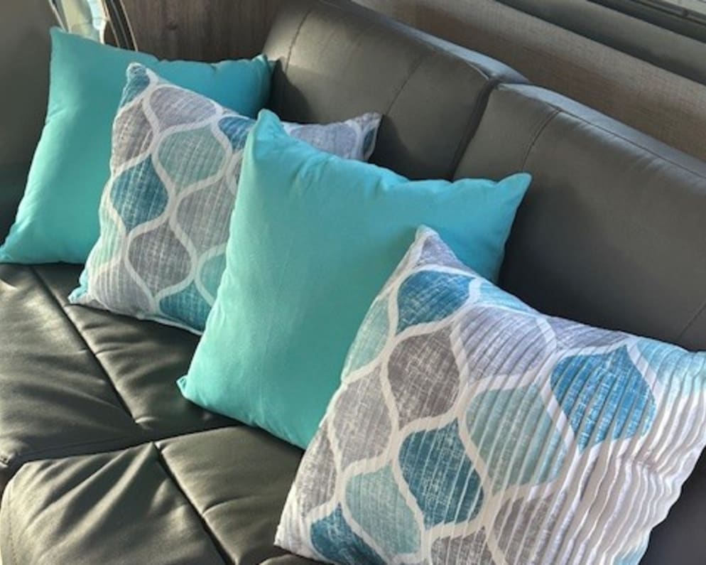 Stylish **RV rental** interior: dark couch with vibrant teal & patterned throw pillows. Ready for travel comfort!