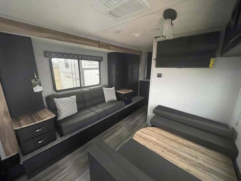 Living/dining room with a large TV, couch with a center console with USB ports and light up cup holders. Couch also pulls out into a bed.. Forest River Freedom Express 246rks 2022