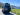 Scenic RV rental on California's coast: A gray camper van parked on a sunny road, overlooking ocean cliffs and mountains.