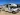 A white and tan Coachmen Class C RV, ideal for an rv rental, is parked outdoors on a sunny day.