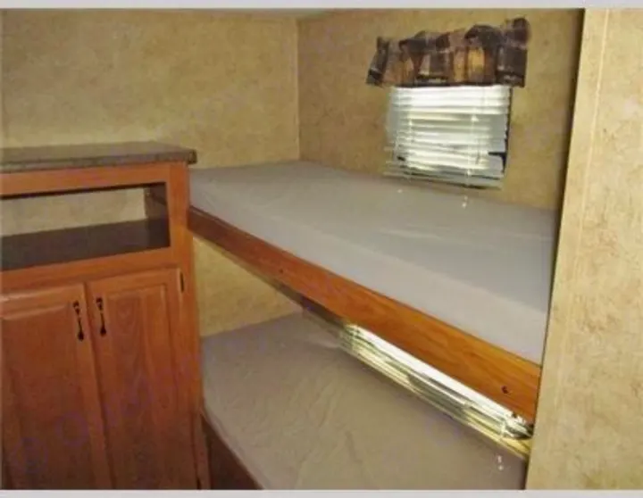 RV rental bunk beds: two mattresses on wooden frames, a window with blinds, and a wood cabinet.. Keystone Laredo 2012