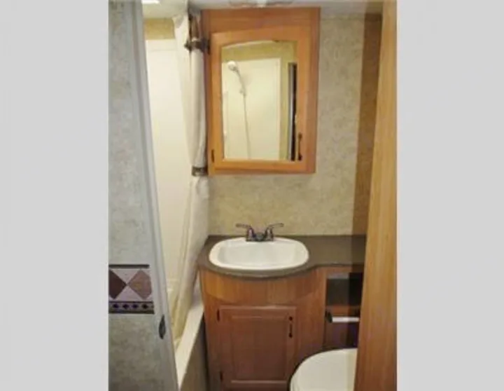 Inside an RV rental, this compact bathroom features a shower, sink vanity, and mirrored medicine cabinet. Functional space.. Keystone Laredo 2012