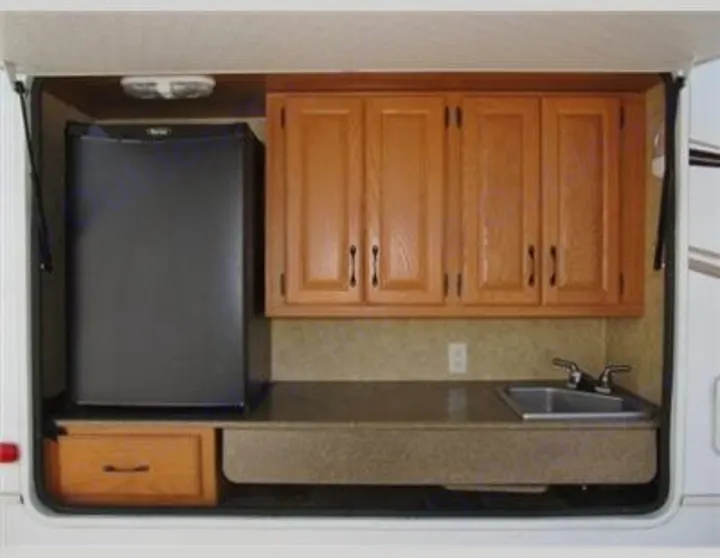 RV rental outdoor kitchen with mini-fridge, sink, and wood cabinets, perfect for camping.. Keystone Laredo 2012