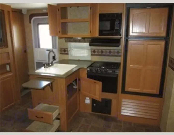 Inside an RV rental: a well-equipped kitchen featuring a sink, gas range, microwave, refrigerator, and ample storage.. Keystone Laredo 2012