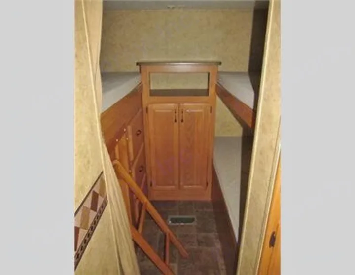 Cozy RV rental bunkhouse showing a central wood cabinet, built-in lower and upper bunks, and a small access ladder.. Keystone Laredo 2012