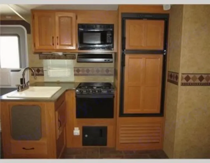 RV rental kitchen: Sink, microwave, gas stove, and integrated fridge offer a practical setup for road trips.. Keystone Laredo 2012