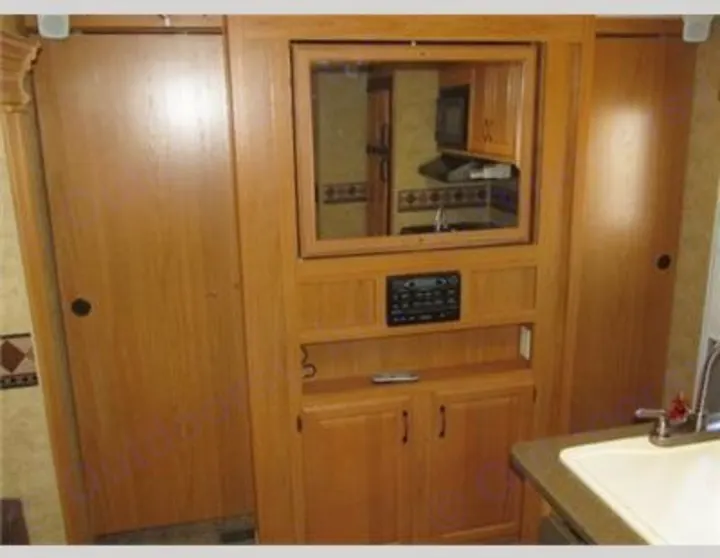 RV rental interior: wood-paneled living space with entertainment center (mirror showing kitchen), storage, and bathroom sink.. Keystone Laredo 2012