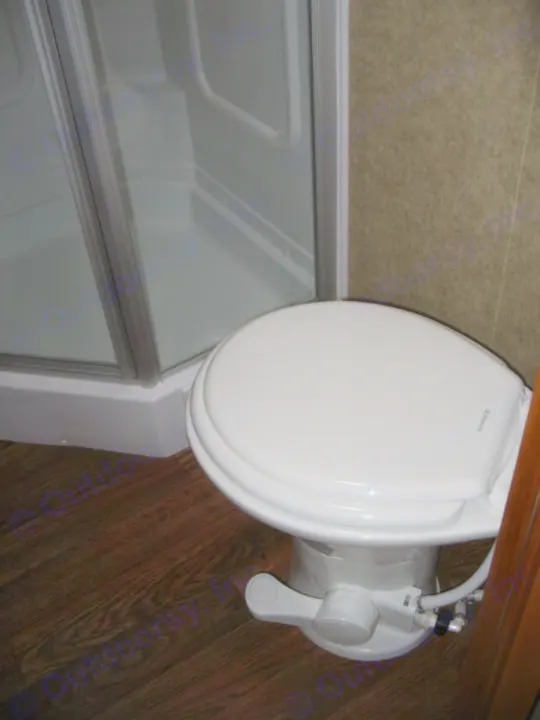 Inside an RV rental: a compact bathroom featuring a white toilet with foot flush and a glass-enclosed shower stall.. Eclipse Milan 2011
