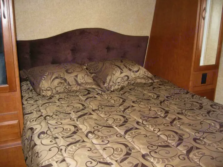 A cozy RV rental bedroom featuring a patterned bed, dark headboard, and wood cabinetry with a mirrored closet.. Eclipse Milan 2011