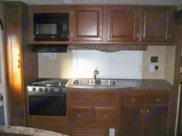 Inside an RV rental: a compact kitchen with microwave, stove, sink, and dark wood cabinetry.. Eclipse Milan 2011