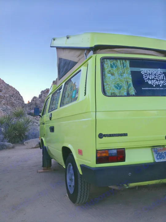 Lime green VW pop-top camper van **rv rental** parked in a serene, rocky desert landscape at dusk.. Volkswagen westfalia 1984