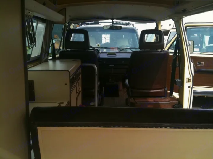 Inside a classic camper van from the rear. Features a kitchen unit left, brown front seats, dashboard, and open doors. Ideal for RV rental.. Volkswagen westfalia 1984