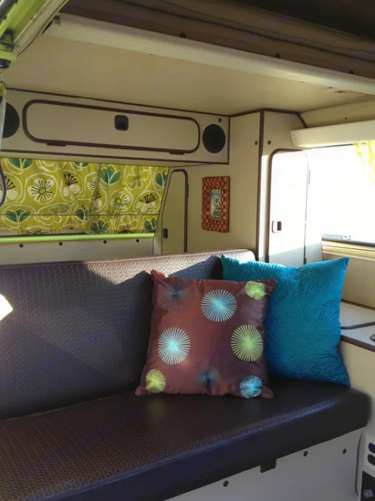 Enjoy the cozy interior of this RV rental, featuring a dark bench seat, decorative pillows, and charming green curtains.. Volkswagen westfalia 1984