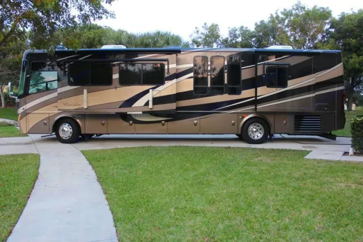 This large, luxurious Class A motorhome, ideal for RV rental, is parked on a driveway with its slide-outs extended.. Thor Mandalay 2006