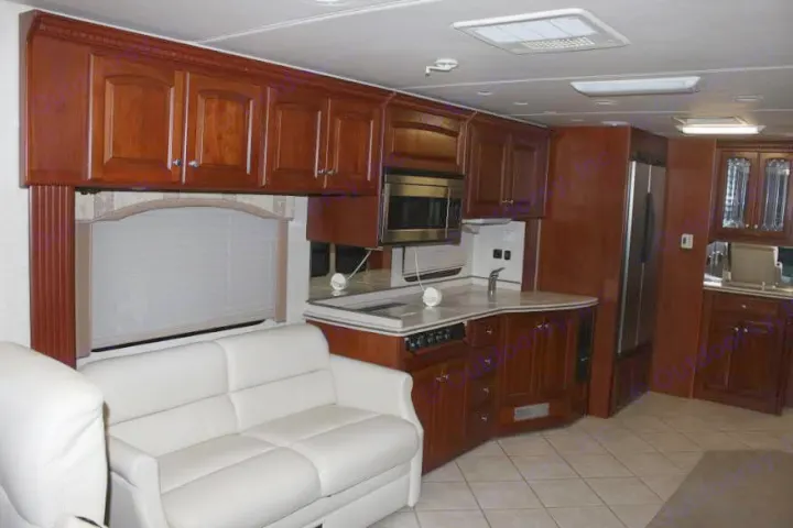 Spacious RV rental interior featuring a full kitchen with dark wood cabinets, modern appliances, and a comfortable white sofa.. Thor Mandalay 2006