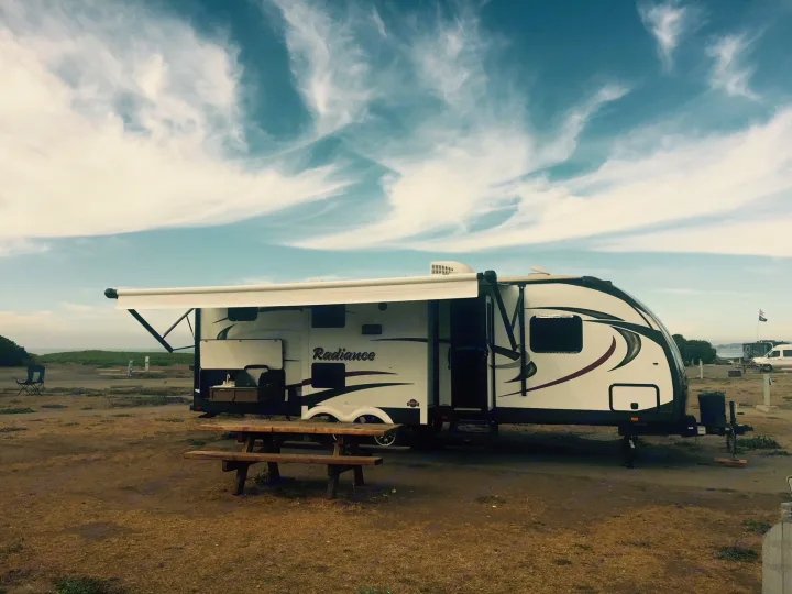 Spacious RV rental with an extended awning and outdoor kitchen at a scenic campsite, complete with a picnic table.. Radiance 28BHIK 2016