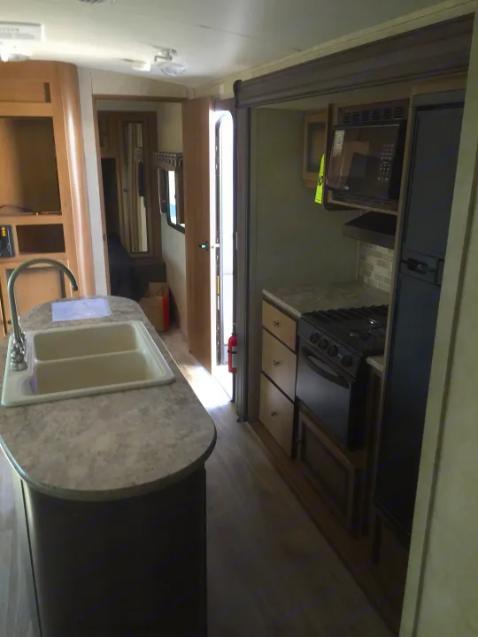RV rental interior: A functional kitchen with sink, microwave, stove, and fridge, showing living space and main entry.. Radiance 28BHIK 2016