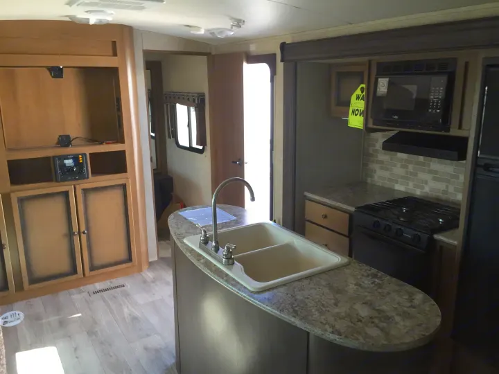 Spacious RV rental interior featuring a modern kitchen with stove, microwave, fridge, and entertainment center.. Radiance 28BHIK 2016