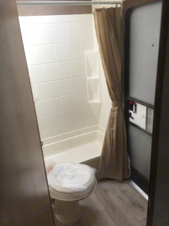 RV rental bathroom: Compact white shower/tub with tiled walls, toilet, and brown shower curtain. Screen door on right.. Radiance 28BHIK 2016