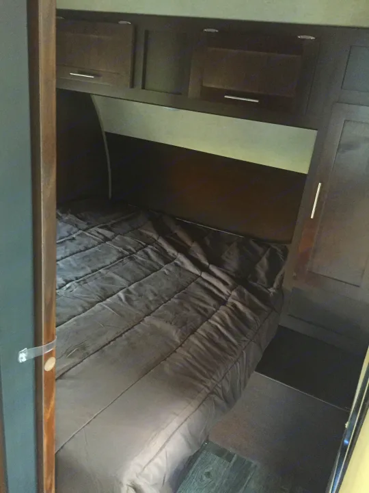 Cozy RV rental bedroom with dark quilted bed, overhead storage cabinets, and wardrobe.. Forest River Cherokee Grey Wolf 2016