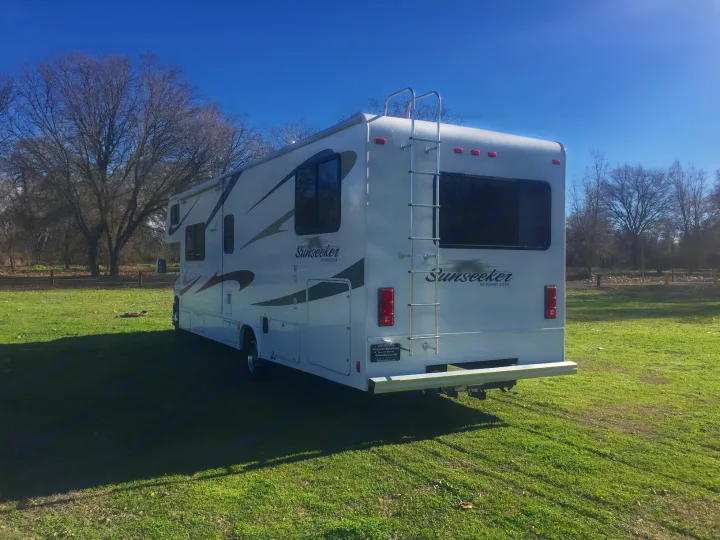 White Sunseeker RV rental parked on green grass under a clear sky. Perfect for your outdoor travel adventure!. Forest River Sunseeker 2012