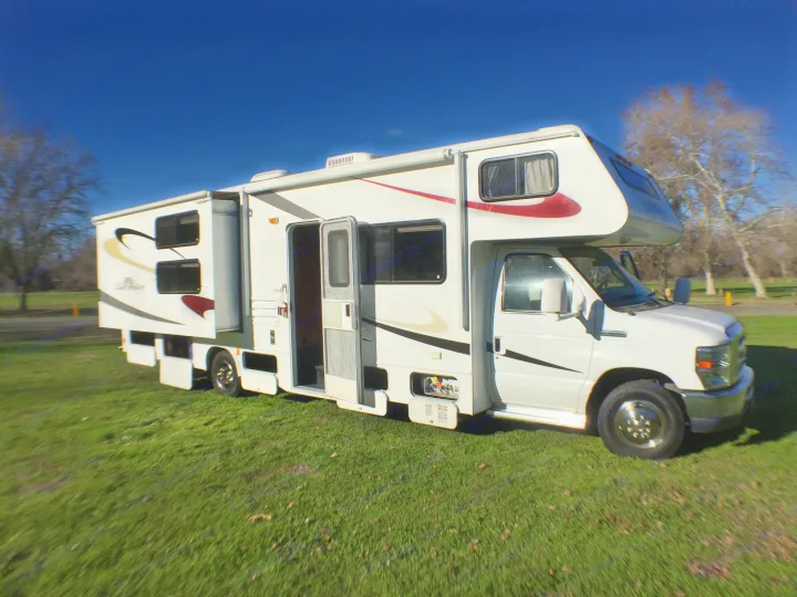 A white Class C RV rental with slide-outs extended, parked on green grass under a clear blue sky.. Forest River Sunseeker 2012