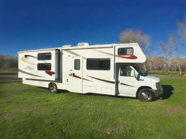White Class C RV rental with slide-out, parked on bright green grass under a clear blue sky.. Forest River Sunseeker 2012