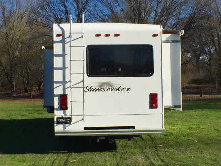 Rear view of a white Sunseeker RV rental parked on green grass, ready for travel. Features a ladder, window, and extended slide-outs.. Forest River Sunseeker 2012