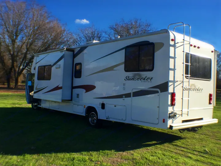 Spacious white RV rental, a Sunseeker motorhome, parked on green grass. Features extended slide-out and ladder.. Forest River Sunseeker 2012