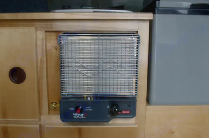 An RV rental amenity: a compact Wave catalytic heater, integrated into the wooden interior, for cozy travel warmth.. Chevrolet Express G1500 AWD 2014