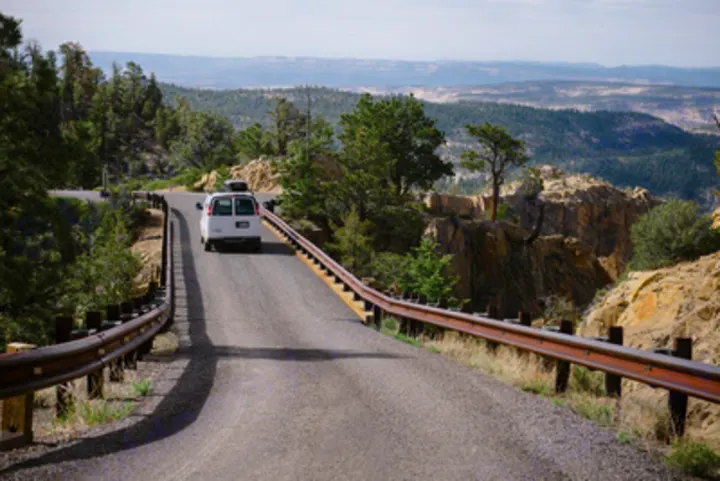 RV rental on a winding mountain road, with guardrails, trees, and scenic cliff views. Perfect road trip!. Chevrolet Express G1500 AWD 2014