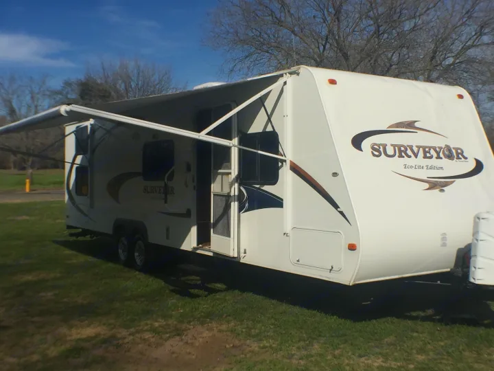 White Surveyor Eco-Lite RV rental with awning extended, ready for camping trips on a grassy site.. Forest River Surveyor 2011