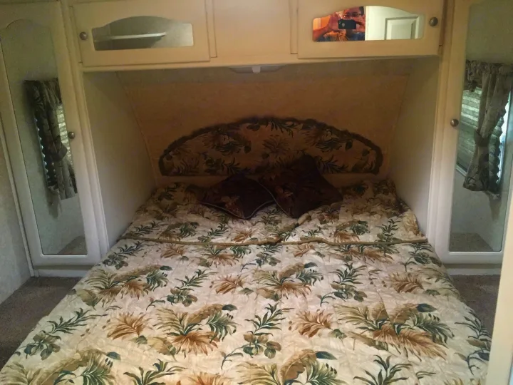 Inviting RV rental bedroom with tropical-patterned bed, headboard, overhead storage, and mirrored closets for a cozy stay.. Keystone Outback 2007