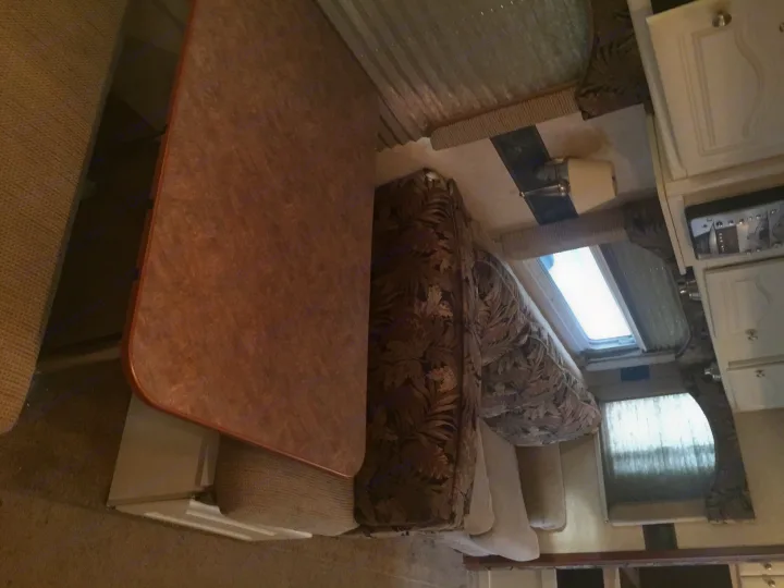 Cozy RV rental interior showing a dinette with a table and bench seating, a sofa, and overhead cabinets.. Keystone Outback 2007