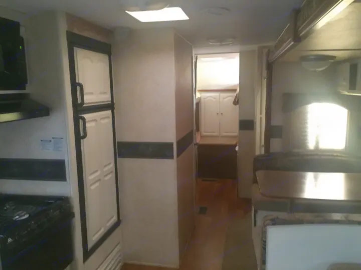 Explore the inviting interior of this RV rental, featuring a functional kitchen, hallway, and a comfortable bedroom.. Keystone Outback 2007