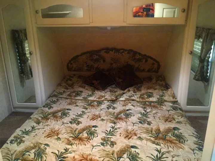 Cozy RV rental bedroom with tropical bedding, built-in cabinets, and mirrored walls for a spacious feel.. Keystone Outback 2007