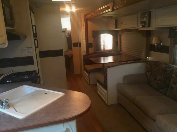 RV rental interior: well-appointed kitchen, cozy dining booth, and living room sofa. A hallway leads to convenient bunk beds.. Keystone Outback 2007