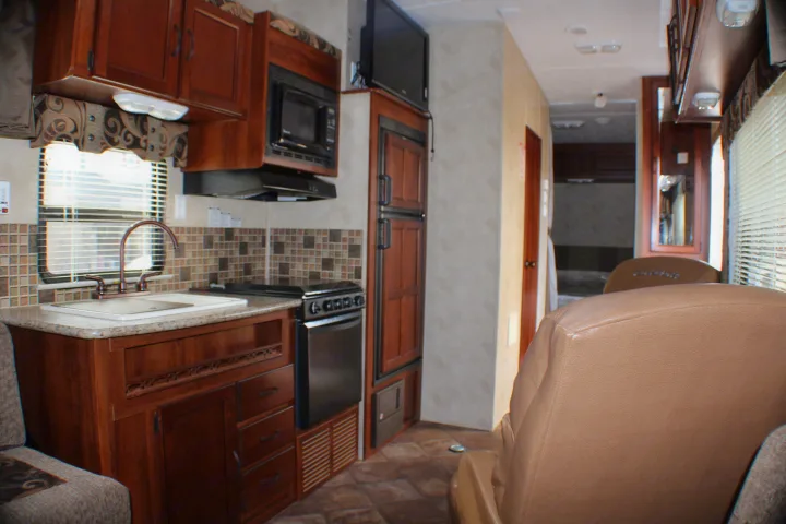 RV rental interior: A well-equipped compact kitchen with sink, stove, microwave, fridge, and seating, ideal for travel comfort.. Palomino Puma Unleashed 2013
