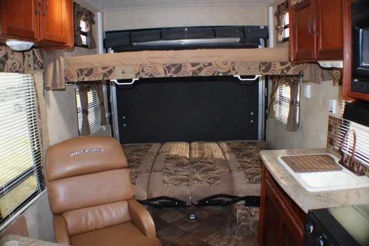 RV rental interior with convertible bunk beds (upper raised, lower seating/bed), 'UNLEASHED' recliner, and kitchen with sink.. Palomino Puma Unleashed 2013