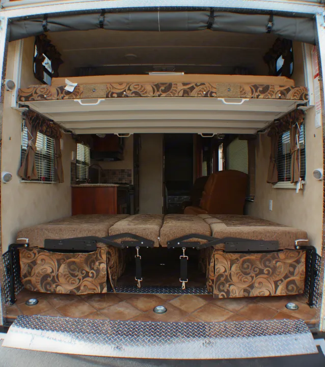 Inside this RV rental toy hauler: a versatile garage space with convertible beds, an upper bunk, and kitchen view.. Palomino Puma Unleashed 2013