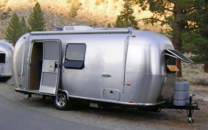 A parked silver Airstream travel trailer, ideal for an rv rental, with its door open in an outdoor setting.. Airstream Safari 2008