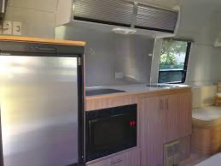 Modern RV rental interior: sleek kitchen with stainless steel fridge, microwave, and wood cabinets, ideal for travel.. Airstream Safari 2008