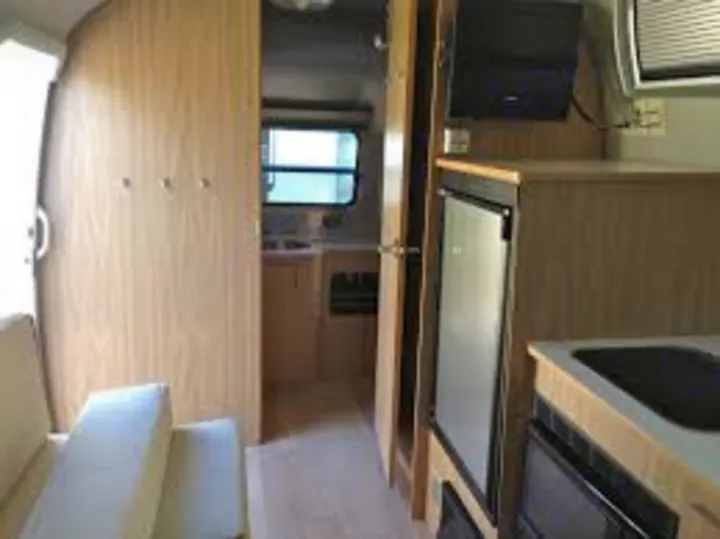 Explore this RV rental's compact interior, featuring a bright seating area and a well-equipped kitchen with a sink & fridge.. Airstream Safari 2008