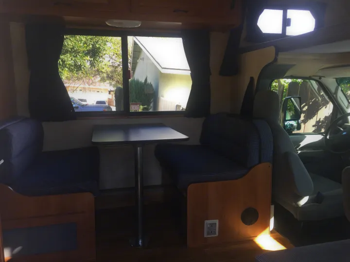 RV rental interior featuring a cozy dinette area with blue benches, a table, and the driver's cabin in view.. Ford Majestic 23A 2012