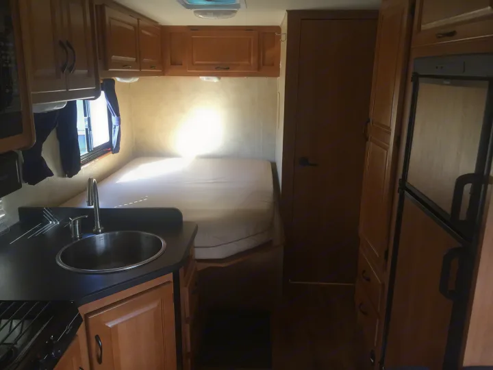 This rv rental interior showcases a compact living space with a kitchen (sink, stove), bed, and refrigerator.. Ford Majestic 23A 2012